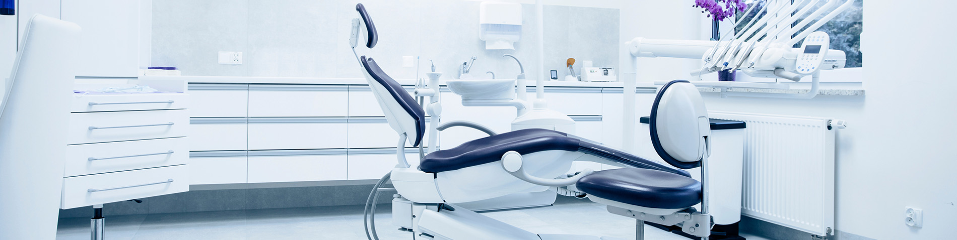 The image shows a modern dental clinic interior with various pieces of equipment, including a dental chair and an X-ray machine.