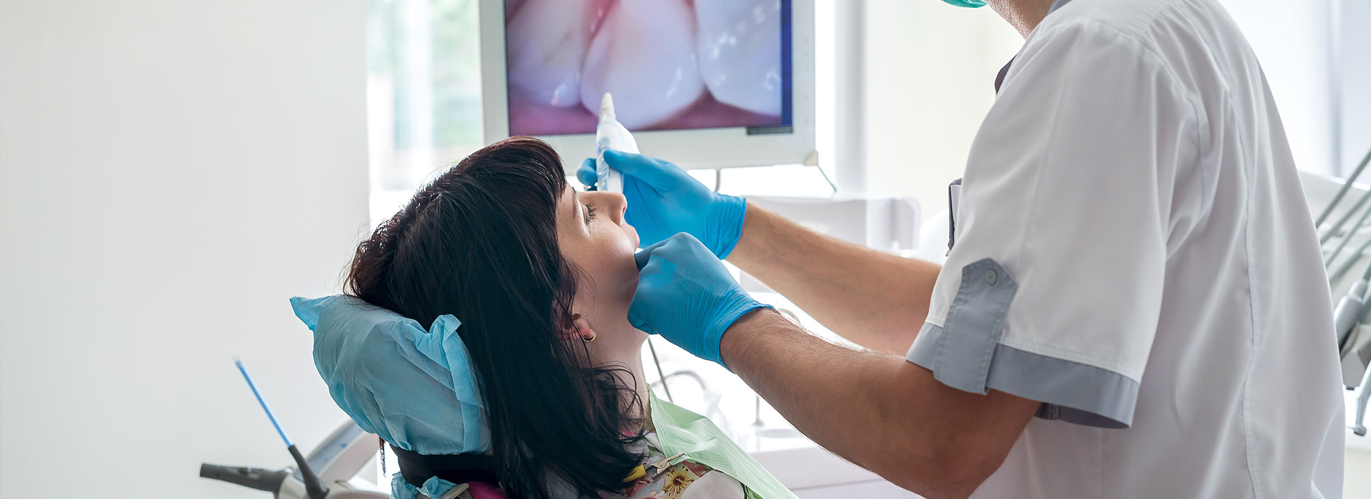 The image shows a dental professional performing oral care on a patient, with proper protective equipment such as gloves and a face mask being worn by both parties.